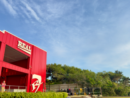 Wetsuits drying against a red barn
